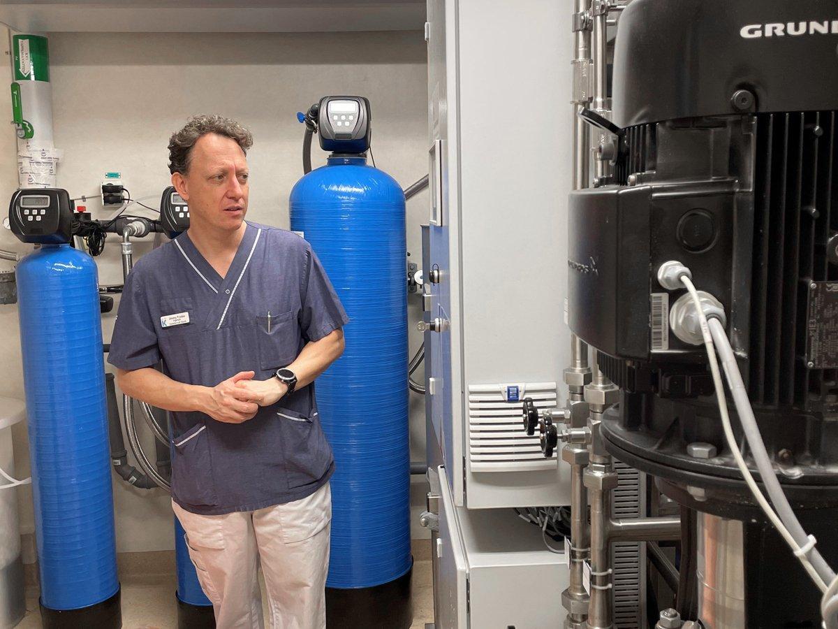 Foto på en man klädd i sjukhuskläder. Han står bredvid en dialysmaskin. 