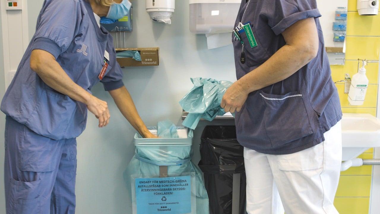 Två personer slänger blåa skyddsförkläden i utpekad korg för återvinning